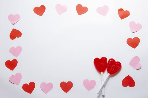 A top view of red and pink hearts with two heart-shaped lollipops on a white table - the concept of Valentine