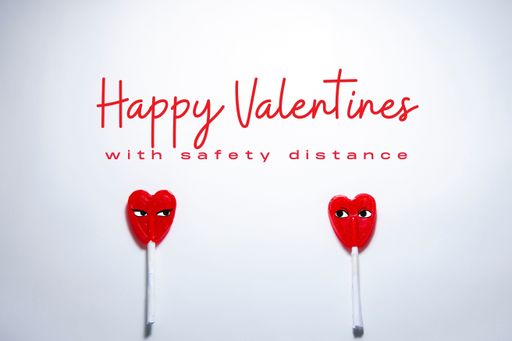 The two heart-shaped lollipops on a white table with "Happy Valentines with safety distance" writing - the concept of new normal