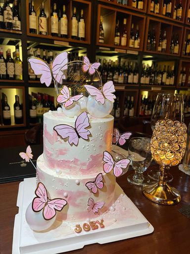A vertical shot of birthday two tier vanilla cake decorated with pink butterflies and name Joey on the base
