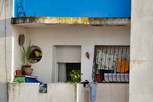 A balcony of a white building with plants and pictures and colorful clothes hanging on the window