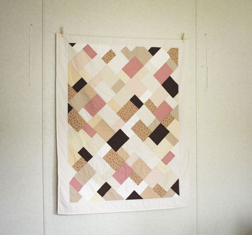A multicolored patchwork quilt hangs on a wall, draped over a patterned rug