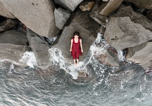 A top shot of a woman in a red dress laying on a huge rock on the sea coast