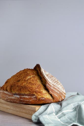 A vertical shot of whole sourdough bread crust with ridge on cloth napkin in turquoise tones