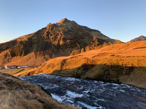 A scenic drone shot of the Skogafoss waterfall in Iceland surrounded with wide fields and hills