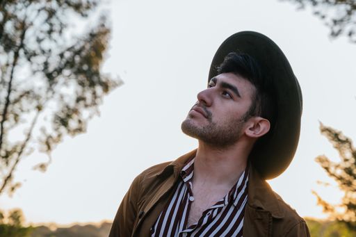 A young Hispanic man with hat and coat enjoying sun rays on a sunny day