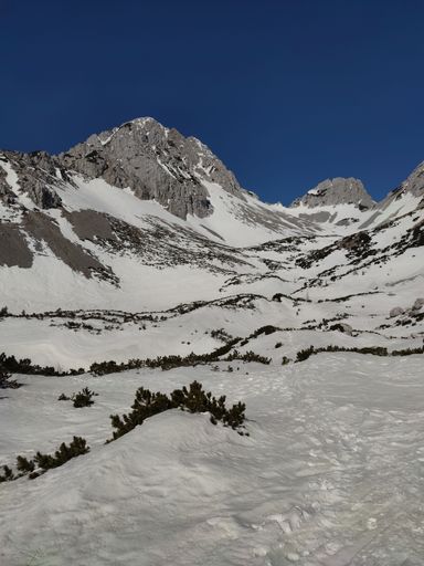 A vertical shot of rocky mountains covered in snow under a blue sky