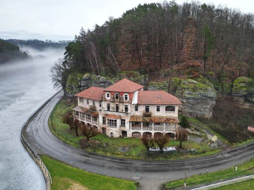 A drone view of an abandoned mansion near a frozen river covered in the fog in the Czech Republic