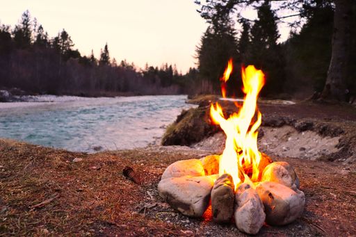 A closeup of a small campfire near a river in a forest in the evening