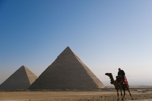 A camel rider in front of The Great Pyramids of Giza against the clear blue sky