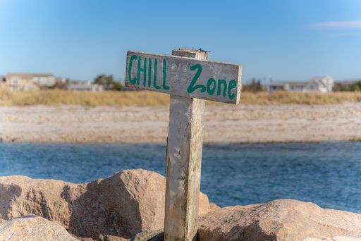 Horizontal photo, image of a wooden sign with post at a beach with water that says CHILL ZONE.