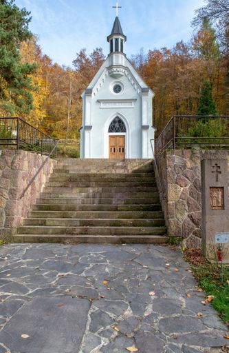 A vertical shot of the white pilgrim's Chapel of the Virgin Mary in the beautiful garden in Kohutovo, Nova Bana, Slovakia