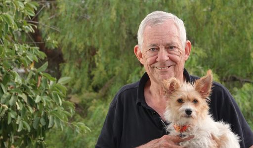 A closeup of a smiling elderly man holding a wire-haired terrier in the park
