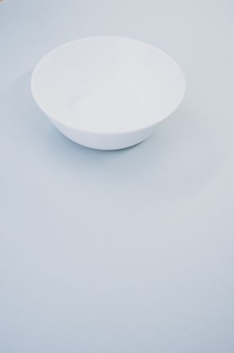 A vertical closeup shot of an empty white glass bowl on a yellow background