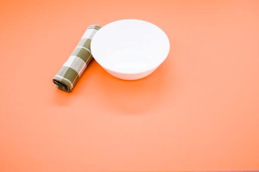 A high angle shot of an empty white plate and a blanket next to it on an orange background