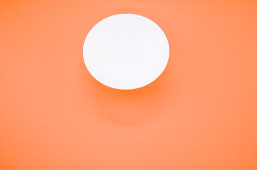 An overhead shot of an empty white glass bowl on an orange background