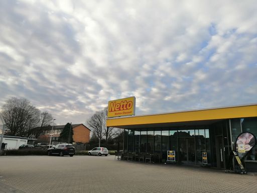 A facade of the Netto Marken Discount supermarket and parking lot under cloudy sky