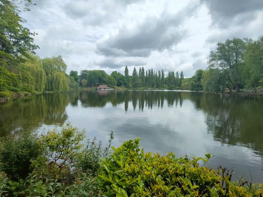 A beautiful park with a small lake surrounded with tall green trees