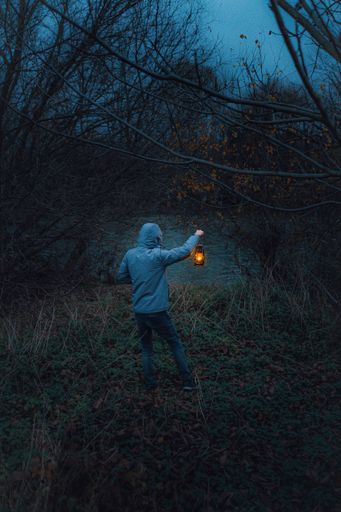 A back view of a young male with a lantern standing in front of a river on a spooky, scary evening