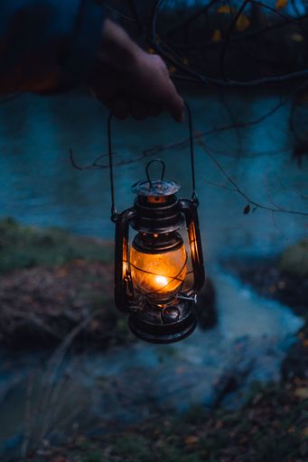 A vertical shallow focus shot of a human hand holding a beautiful lantern above the river