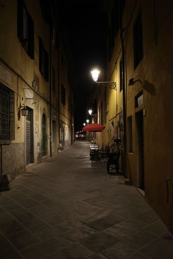A vertical shot of a narrow street at night illuminated with lights on the walls of the buildings