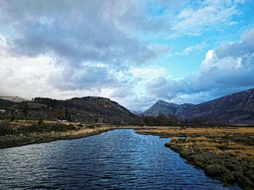 A scenic shot of a river flowing through the Scottish highlands under the cloudy sky