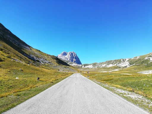 An empty road amidst snowcapped mountains against a clear blue sky.