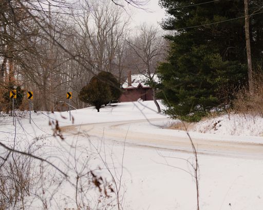 A winding snow-covered road leading to a rural house, with road signs and trees, in Michigan US