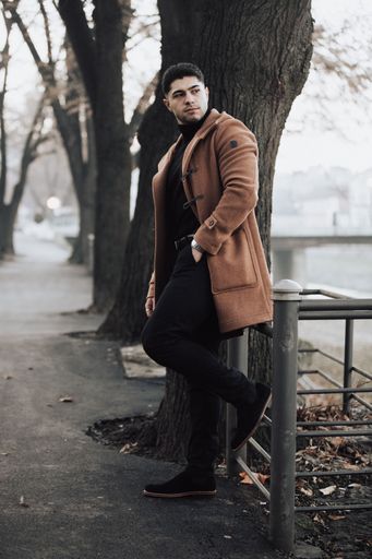 A young, fashonable man in classy winter coat posing next to a tree, vertical