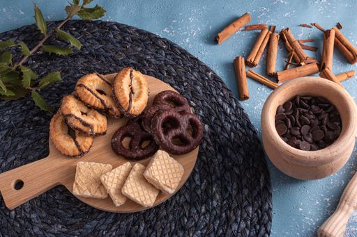 A top view shot of shortbread and chocolate cookies, wafers, chocolate chips, and cinnamon sticks scattered on the tabl