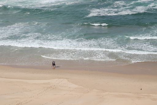 An aerial shot of two tourists walking along the beautiful sandy shore