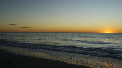 A sandy beach by gray dunes sea and golden sunset sky on the horizon, perfect for background