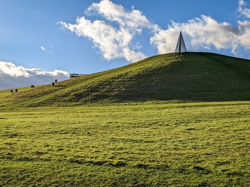 A grass meadow field with green hill under blue cloudy sky, perfect for background