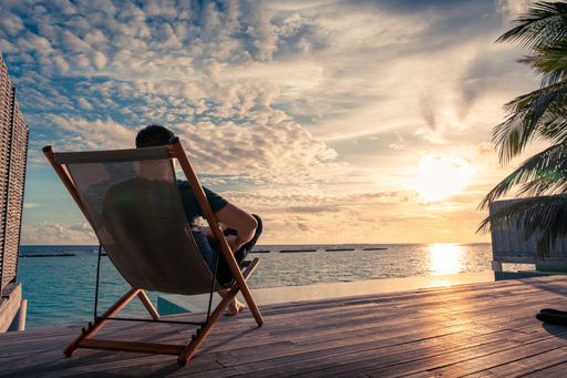 A Young man sitting on a patio chair and enjoying the sunset over the ocean in the Maldives.