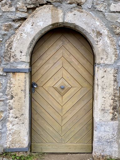 A vertical shot of an old stone-made building facade wit arched doorway and wooden door