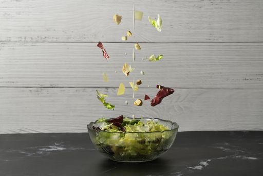 A vertical shot of a sliced homemade caesar salad with fresh flying ingredients on a kitchen table