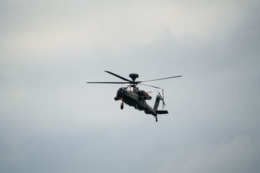 A dark grey army attack helicopter in flight during the daytime