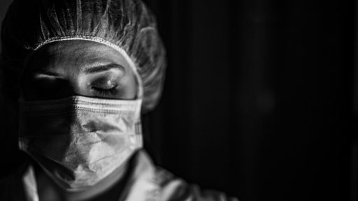 A grayscale closeup of a female healthcare worker wearing a mask on a black background