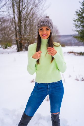 A portrait of a young pretty brunette female wearing a light green sweater and a wool hat