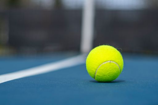 A closeup of a tennis ball on the court on a sunny day with a blurry background