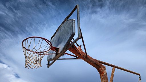 A low angle shot of a basketball hoop in the playground on blue cloudy sky background