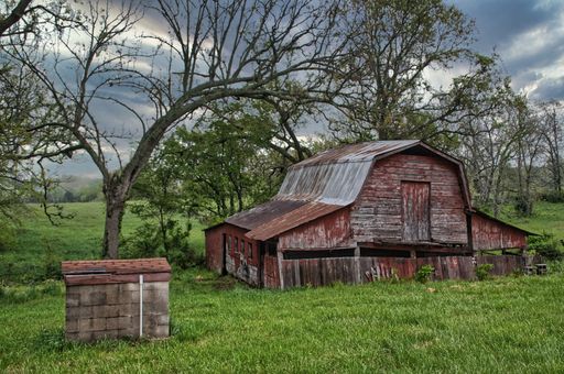 A beautiful view of an old wooden barn in a green field with trees