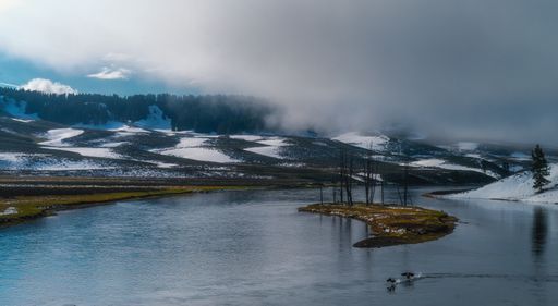A mysterious shot of a beautiful lake surrounded by a snowy foggy forest in a daytime