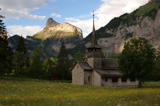 A scenic view of an old church located in a field surrounded by mountains in Kandersteg, Switzerland