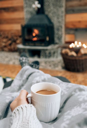 A shallow focus shot of hands holding a mug of coffee on fireplace background