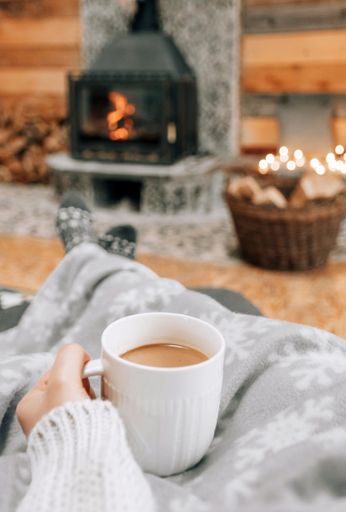 A shallow focus shot of hands holding a cup of coffee on fireplace backgroun
