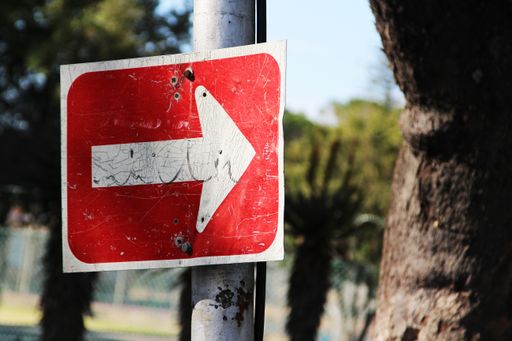 A closeup shot of a red sign pointing to the right in front of the trees