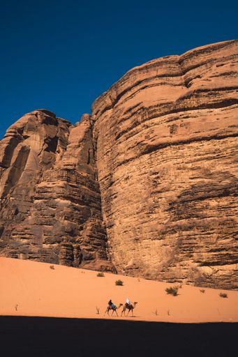 A vertical shot of two men in traditional Arab clothing riding camels in the desert in Wadi Rum, Jordan