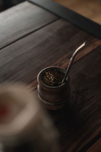 A vertical shot of mate tea in a wooden mate cup with a metal straw on a wooden surface