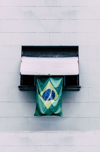 A vertical shot of the  Brazil flag hanging on the window of a wall