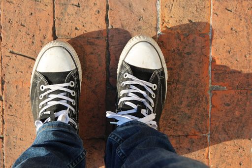 A high angle shot of a person's feet on the tiled pavement under the sun light
